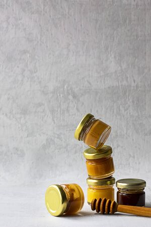 Five Small glass jar with metal cap with different kinds and colours of honey one on another and spoon isolate and on grey cement background with copy space. Healthy product, natural. Verticalの写真素材