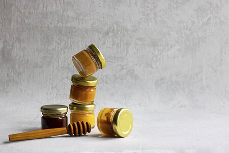 Five Small glass jar with metal cap with different kinds and colours of honey one on another and spoon isolate and on grey cement background with copy space. Healthy product, natural. Horizontalの写真素材