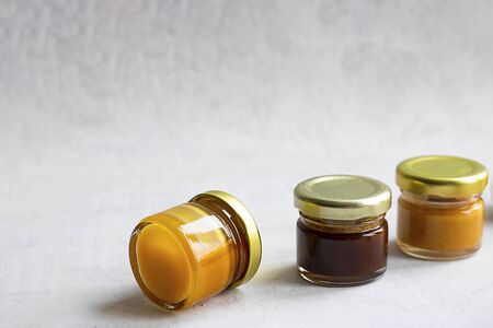 Three Small glass jar with metal cap with different kinds and colours of honey put in line isolate and on grey cement background with copy space. Healthy product, natural. Horizontalの写真素材