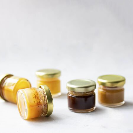 Five Small glass jar with metal cap with different kinds and colours of honey put in line isolate and on grey cement background with copy space. Healthy product, natural. Squareの写真素材