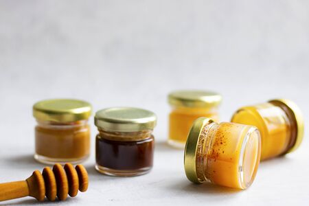 Five Small glass jar with metal cap with different kinds and colours of honey put in line and wooden spoon isolate and on grey cement background with copy space. Healthy product, natural. Horizontalの写真素材