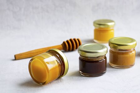 Four Small glass jar with metal cap with different kinds and colours of honey put in line and wooden spoon isolate and on grey cement background Healthy product, natural. Horizontal