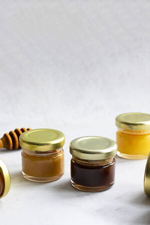Five Small glass jar with metal cap with different kinds and colours of honey put in line and wooden spoon isolate and on grey cement background with copy space. Healthy product, natural. Verticalの写真素材