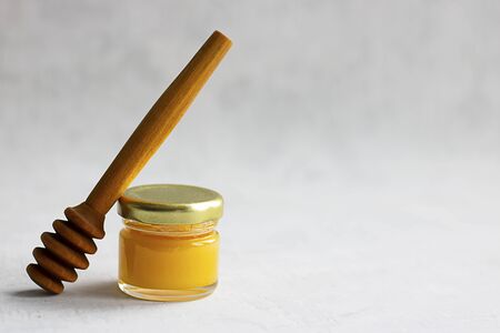 Small glass jar with metal cap with light yellow honey and special wooden spoon isolate on grey cement background with copy space. Healthy product, natural, Horizontalの写真素材