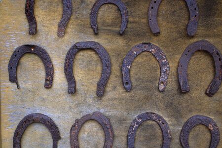 Lines on many old rusty metal horseshoe hanging on an old wooden surface. Horizontalの写真素材