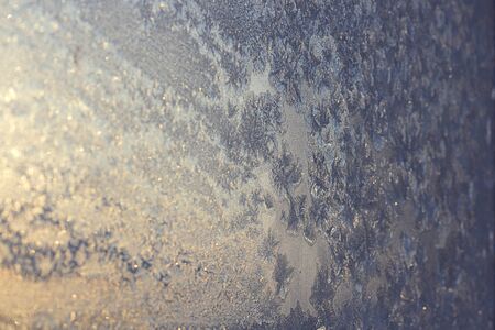 Ice patterns on winter glass of window, with the light seen through it. Horizontal. Selective focus. Creative background about winter, cold, christmas time.の写真素材