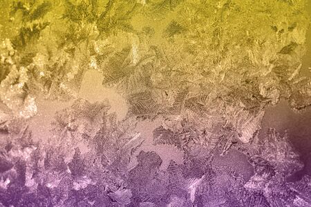 Ice patterns on winter glass of window, with the light seen through it. Light yellow and violet duotone. Selective focus. Creative background about winter, cold, christmas time. Horizontal banner.の写真素材