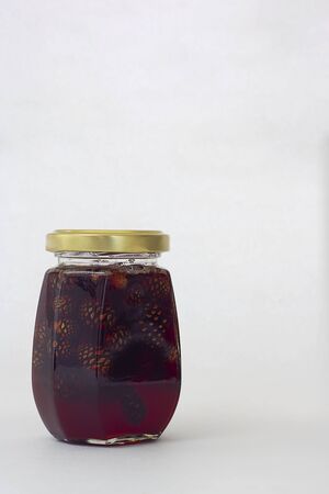 Glass jar with yellow gold metal cup with pine cone jam isolated on white. Vertical with copy space.の写真素材