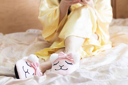 female feet wearing cute llama trendy pink slippers, lay on bed with wooden headboard and on pastel silk gown. Home Rest Relax Holidays Horizontalの写真素材