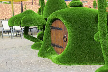 Green sculpture of small house with round wooden door surrounded by mushrooms made from artificial grass.Vertical with copy space. Urban design, city architecture, park decorationの写真素材