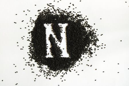 Handful of sweet basil black seeds, letter N uppercase of English alphabet on white background. Black and white. Lettering. Typography. Horizontal. Healthy and super food.の写真素材