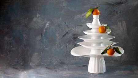 White dishes Pyramid like Christmas tree with mandarins with leaves on top, bunch below on dark Creative concept, dishware, veg, agriculture, vegetable, kitchen, restaurant, postcard, Xmas, New Yearの写真素材