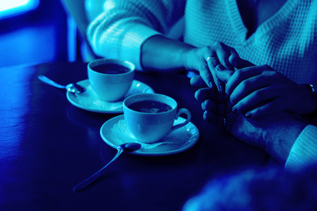 man and woman hold hands, close up of couple's arms on wooden table in restaurant, two cups. date,...