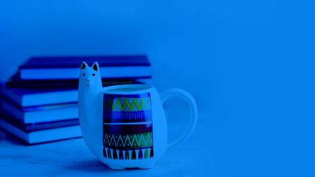White Llama mug with pile of books on light empty background, horizontal with copy space for text or design. Trendy animal accessories for school and office. Classic, blue monochrome, trend 2020の写真素材