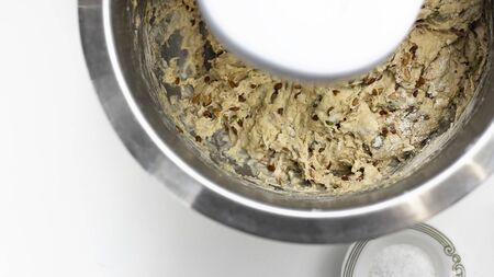 Raw sour dough whole wheat bread with seeds, prosess of mixing pastry in metal bowl, knead, horizontal with copy space, selectuve focus, healthy food, nutritious. White background. Top view.の写真素材