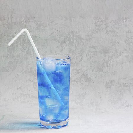 Summer cold drink in tall glass with ice and plastic straw on grey background. Sparkling beverage, alcohol drink, coctail. Classic, blue monochrome, trend 2020. Squareの写真素材
