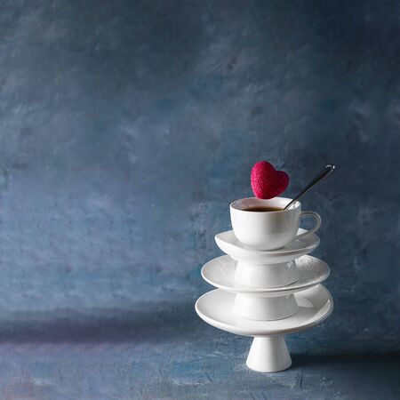 White saucer pyramid with cup of tea on top and flying red hearts candy over it. Creative concept, love, relations, gift, celebrate, restaurant, food levitation, St. Valentine's day. Dark background.の写真素材