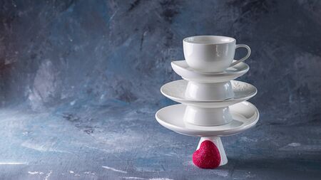 White saucer pyramid with cup on top and one red heart candy on it Dark background. Creative concept, love, relations, gift, celebrate, restaurant, food, St. Valentine's day. Horizontal, copy spaceの写真素材