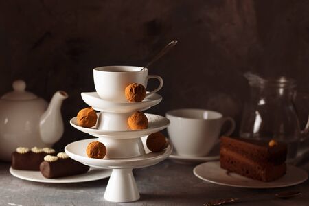 White saucer pyramid with cup of tea on top decorated with chocolate truffles on surved dessert table on dark background. Creative concept, restaurant, candy shop. Horizontal for postcard, wallpaperの写真素材