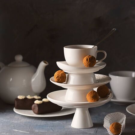 White saucer pyramid with cup of tea on top decorated with chocolate truffles on surved dessert table on dark background. Creative concept, restaurant, candy shop. Square for postcard, wallpaperの写真素材
