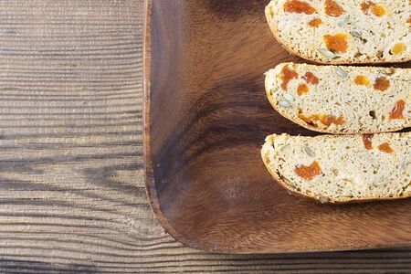 Three pieces of Biscotti with Apricot and Pumpkin seeds on square brown wooden plate on textured bachground, Italian traditional sweet dried bread, homemade cookie. Horizontal top view shot with copy spaceの写真素材