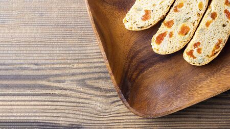 Three pieces of Biscotti with Apricot and Pumpkin seeds on square brown wooden plate on textured bachground, Italian traditional sweet dried bread, homemade cookie. Horizontal banner, top view shot with copy spaceの写真素材