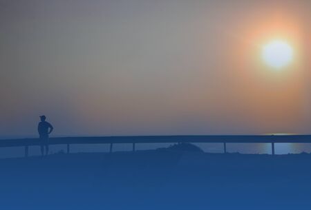 Silhouette of unreconizable man wearing cap near traffic devider on backround of sky. Horizontal, copy space. Classic, blue monochrome, trend 2020. For travelling, meditation, sport.の写真素材