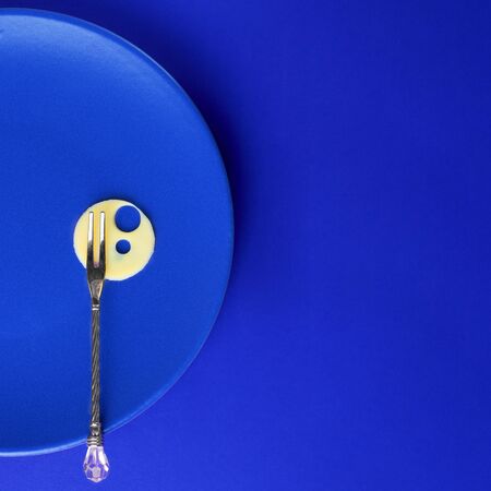 Food concept, Round slice of cheese with holes on plate with small fork on empty background. Square with copy space. Creative for dairy manufacture, diet, health, menu. Classic, monochrome, trend 2020の写真素材