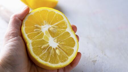 Half of Ugly double organic lemon unusual shape in human hand on grey background with copy space. Buying imperfect product to reduce food waste. Horizontal. Yellow bright color fruit. Eco trendの写真素材
