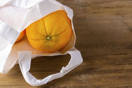 organic orange in white fabtic bag on wooden textured surface with knife. Buying imperfect product to reduce food waste. Horizontal. Yellow bright color fruit. Cooking. Eco trendの写真素材