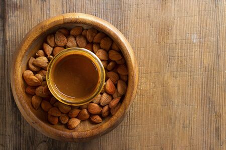 Apricot kernels in round bowl, glass jar with nut butter in center on wooden background. Top view. Food concept with copy space. Product for cardio vascular system, full of vitamims.の写真素材