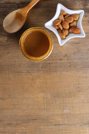 Glass jar with aprikot kernel butter, spoon, star shape bowl with whole nuts on wooden background with copy space. Product is good for cardio vascular system, full of vitamims. Vertical. Top view.の写真素材