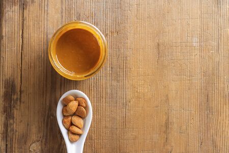 Glass jar of aprikot kernel butter, ceramic white spoon with whole nuts on wooden background with copy space. Product for cardio vascular system, vitamims. Top view. Horizontalの写真素材