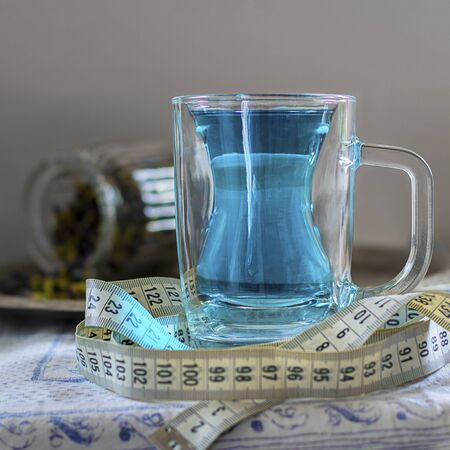 Butterfly pea flower blue tea in glass mug with silhouette like slim woman figure. With measuring tape around as drink helps to loose weight. Healthy thai detox herbal beverage. Squareの写真素材