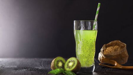 Fresh green vegan beverage in glass with straw with kiwi and basil seeds for health on black bachground with copy space, vegetarian food, dark key. Concept of natural coctail and juice. Detox.の写真素材