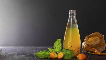 Fresh orange vegan beverage in bottle with cumquat and basil seeds for health on black bachground with copy space, vegetarian food, dark key. Concept of natural coctail and juice. Detox.の写真素材