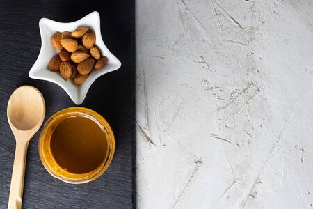Glass jar with aprikot kernel butter, wooden spoon, white star shape bowl with whole nuts and spoon on black shale plate and grey cement background, copy space. Product for cardio vascular systemの写真素材