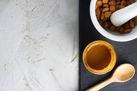Glass jar with aprikot kernel butter, wooden spoon, white mortar with pestle with whole nuts and spoon on black shale plate and grey cement background, copy space. Product for cardio vascular systemの写真素材