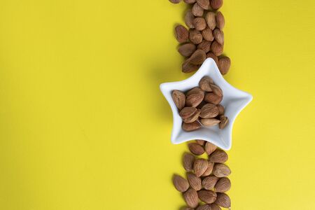 Glass jar with aprikot kernel in white star shape bowl with whole nuts on yellow background, copy space. Copy space. Product for cardio vascular systemの写真素材