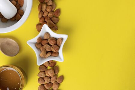 Glass jar with aprikot kernel butter, wooden spoon, white star shape bowl with whole nuts and spoon on yellow background, copy space. Product for cardio vascular systemの写真素材