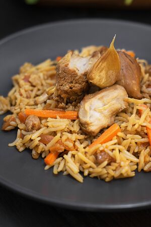 Traditional pilaf with turkey and garlic on black plate on dark wooden table. Close up. Vertical. Eastern, uzbek dish made from meat and rise.の写真素材