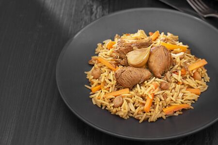 Traditional pilaf with turkey on black plate with knife and fork on dark wooden table. Horizontal with copy space. Eastern, uzbek dish made from meat and rise.の写真素材