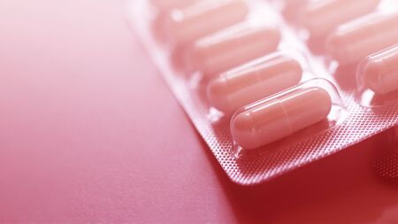 one blister of pills closeup. Oval long shape remedies. Red tone, sun fleck. Background or texture about Medicine, Health, Vitamins which support human body, hepl to immune viruses, infectionsの写真素材