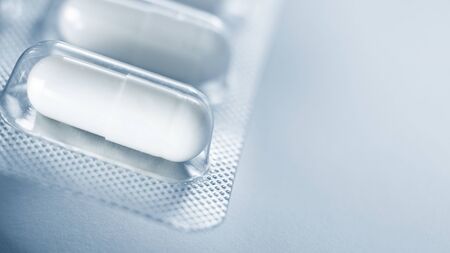 one blister of pills macro. Oval long shape remedies. Blue tone, sun fleck. Background or texture about Medicine, Health, Vitamins which support human body, hepl to immune viruses, infectionsの写真素材