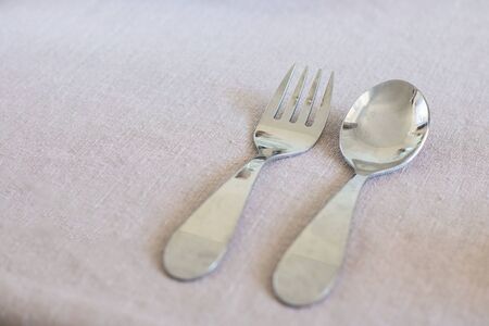 Metal reusable baby spoon and fork on table cloth with copy space. Tableware for kid. Refuse using plastic dishes for children, zero waste. Eco cooking for toddler. Responsible parentsの写真素材