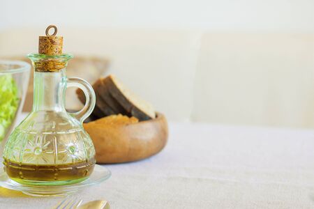 Extra virgin olive oil in beautiful glass bottle on served table with defocused green salad and dark bread. Horizontal copy space. Preparation for meal at home. Organic products, Foodの写真素材