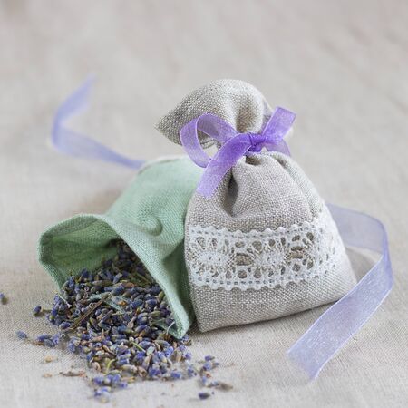 Small linen bag filled with dried lavender decorated with lacework and violet ribbon coque, two sachets, one is opened. Square. Composition on thenatural flaxen background.の写真素材