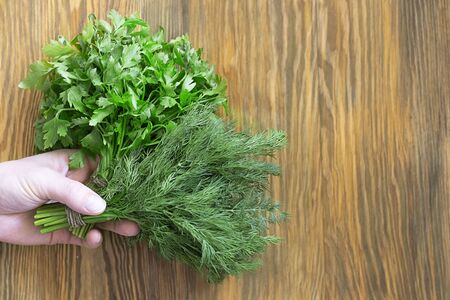 Two bunches of green parsley and dill in hand on textured wooden brown background. Horizontal with copy space. Fresh spices from garden, Healthy greens full of vitamins. Vegan ingredient. Top viewの写真素材