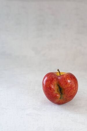 Red organic ugly apple on grey cement background with copy space. Fruit with unusual shape. Buying imperfect product to reduce food waste. Sustainable consumption. Vertical. Fresh food, eco trend.の写真素材