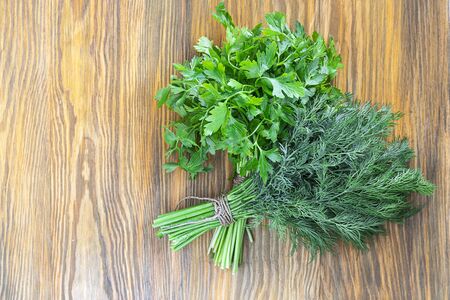 Two bunches of green parsley and dill on brown textured wooden background. Horizontal with copy space. Fresh spices from garden, Healthy greens full of vitamins. Top view. Vegan ingredient.の写真素材
